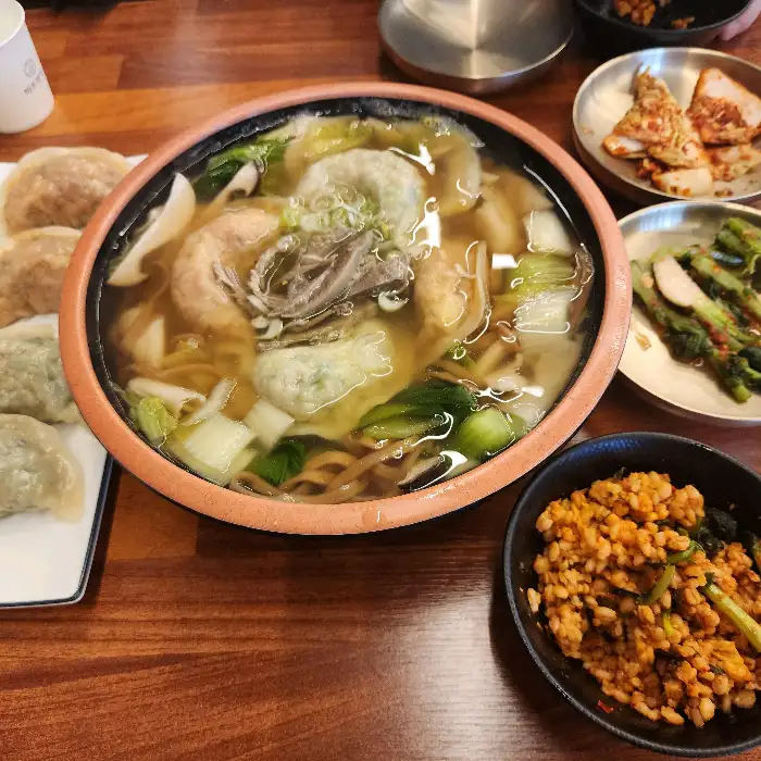 넓은 냄비에 푸짐하게 담긴 칼국수, 수제비, 만두, 고기가 들어간 국물 요리와 곁들여 나온 겉절이, 김치, 밥