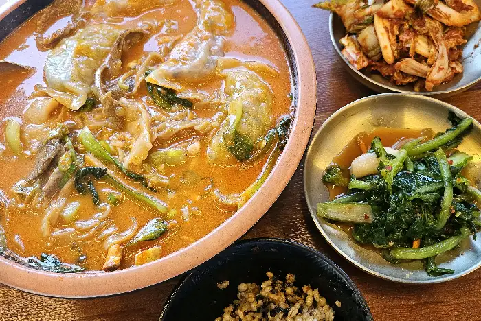 커다란 냄비에 담긴 얼큰한 국물의 모듬 칼국수, 수제비, 만두 요리와 곁들여 나온 여러 종류의 김치와 밥