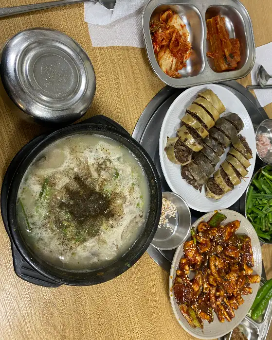 테이블에 차려진 푸짐한 한 상. 가운데에는 순대국밥과 닭발, 그리고 다양한 밑반찬들이 놓여 있습니다.
