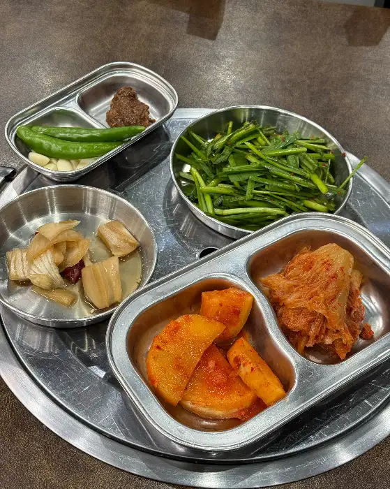 다양한 종류의 밑반찬들. 갓김치, 쌈무, 고추, 마늘 등이 정갈하게 담겨 있습니다.