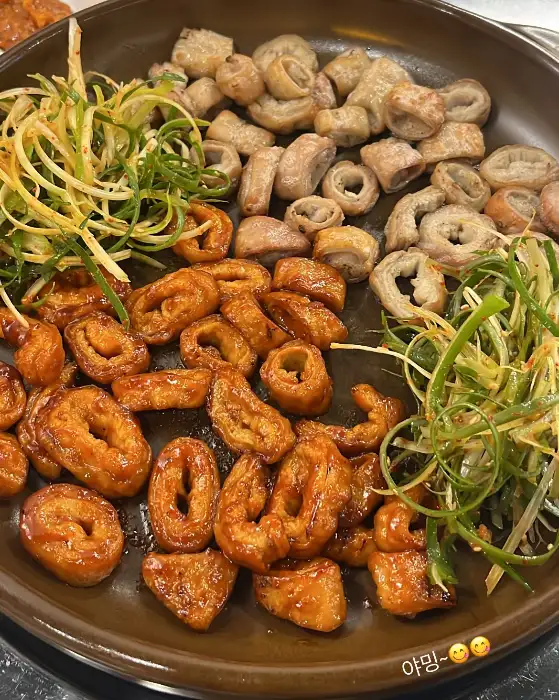 잘 구워진 곱창과 막창이 철판 위에 가지런히 담겨 있으며, 신선한 파채가 곁들여져 있습니다.