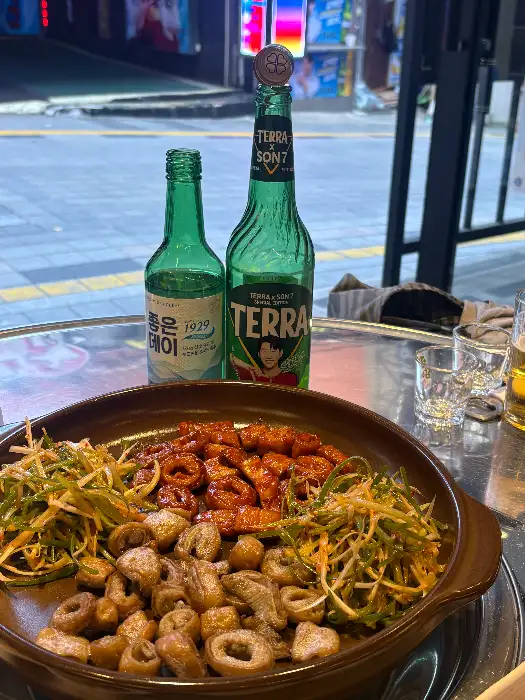 테이블 위에 놓인 두 병의 술병과 잔, 그리고 곱창 구이가 담긴 접시.