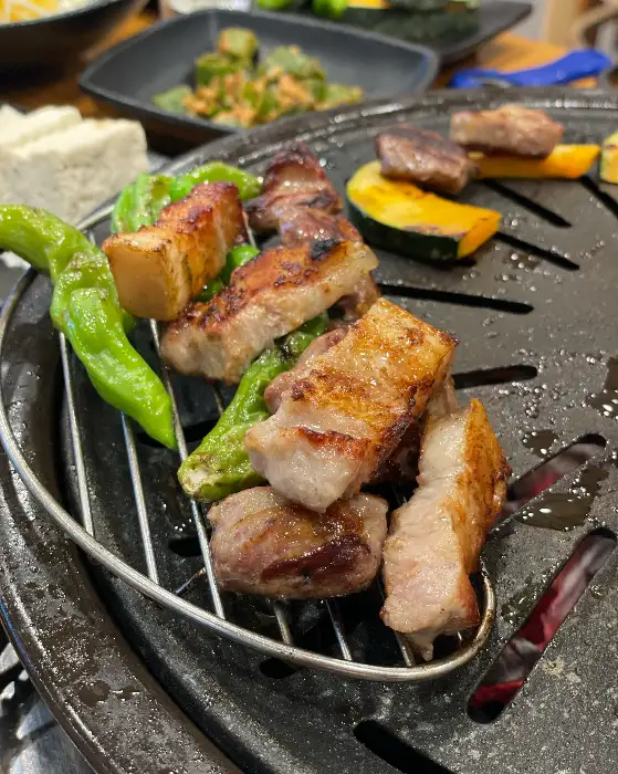 잘 달궈진 불판 위에서 지글지글 구워지고 있는 두툼한 오겹살. 곁들임으로 나온 고추와 단호박도 보인다.