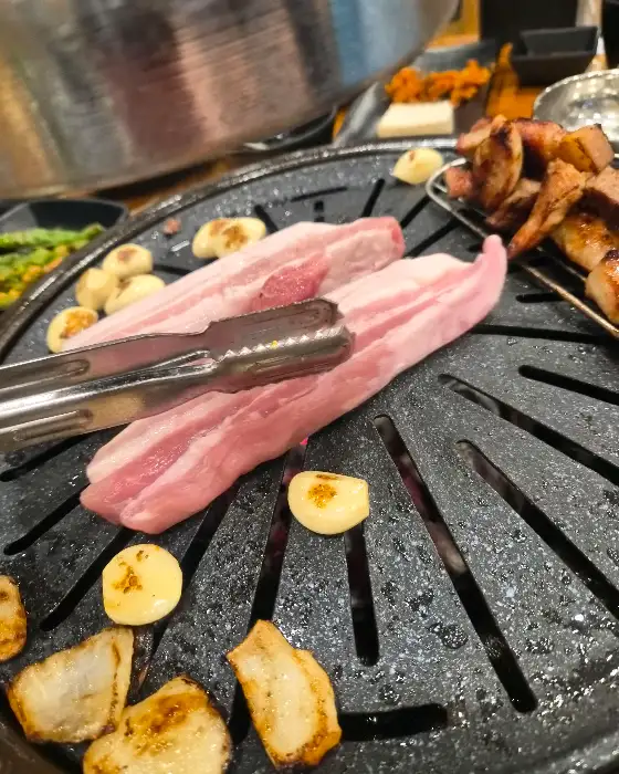 불판 위에 올라가기 전의 신선한 생 오겹살 덩어리와 함께 집게가 놓여있다.