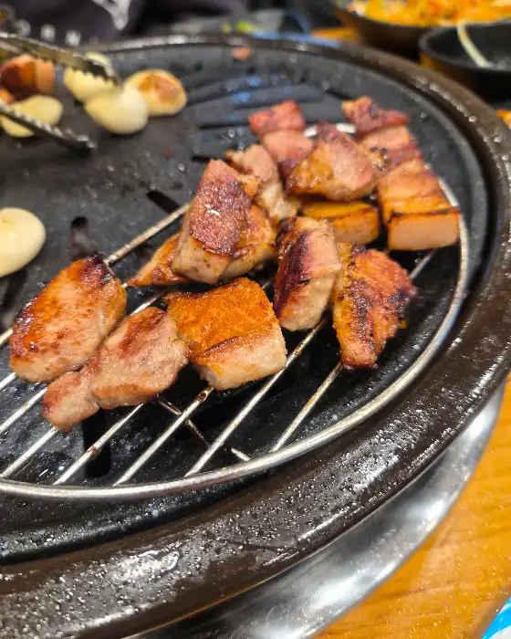 잘 구워진 오겹살 조각들이 불판 위에 가지런히 놓여있는 모습. 먹음직스러운 갈색 빛깔을 띤다.