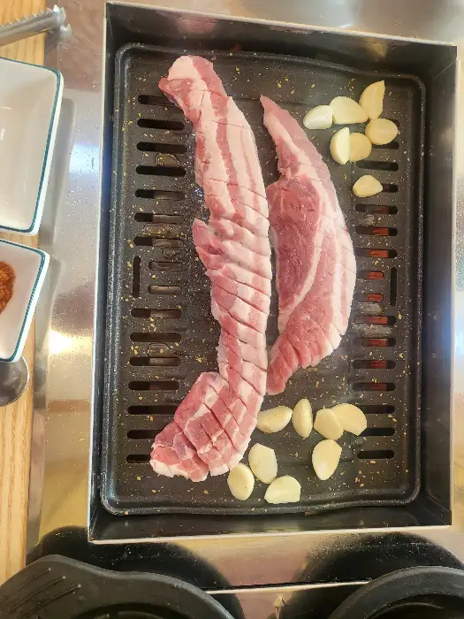 불판 위에 올라가 지글지글 익어가는 삼겹살과 마늘