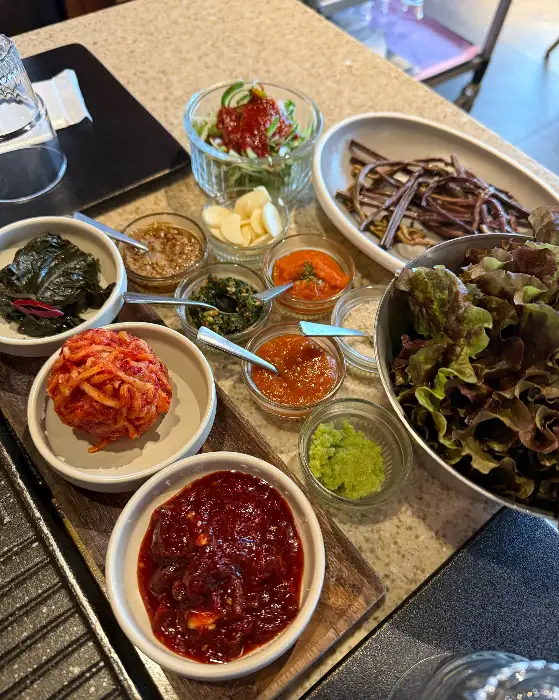 다양한 종류의 소스와 쌈 채소, 그리고 갓 무쳐낸 듯한 신선한 반찬들