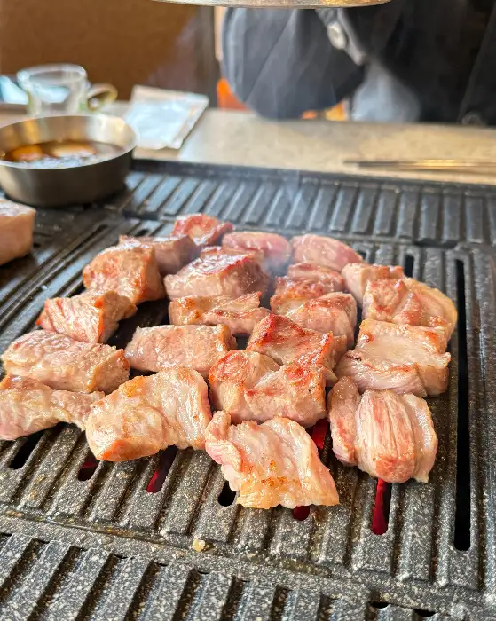 두툼한 흑돼지 오겹살이 불판 위에서 지글지글 익어가고 있는 모습