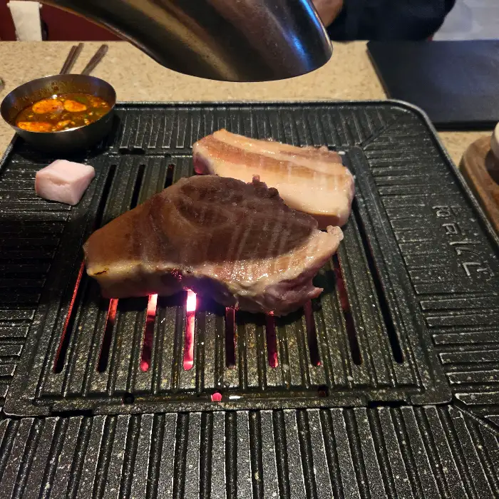잘 익은 흑돼지 목살 한 점이 불판 위에서 맛있게 구워지고 있는 모습