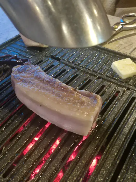 쫄깃해 보이는 흑돼지 오겹살 덩어리가 불판 위에서 익어가고 있는 모습