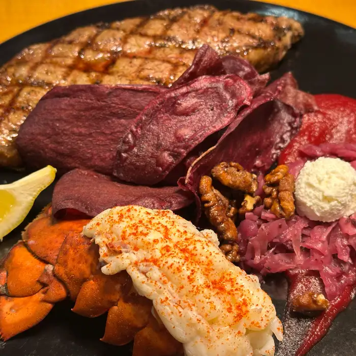 푸짐한 스테이크와 랍스터 테일, 보라색 칩, 그리고 크림치즈가 플레이팅된 고급스러운 요리.