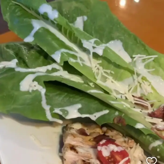 신선한 로메인 상추 위에 뿌려진 드레싱과 베이컨, 치즈가 곁들여진 샐러드.