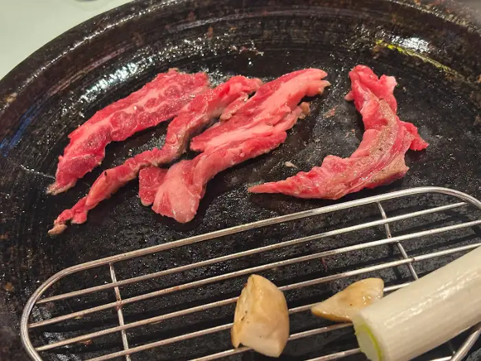 돌판 위에서 구워지고 있는 소고기 조각들, 곁들임 채소들과 함께 있습니다.