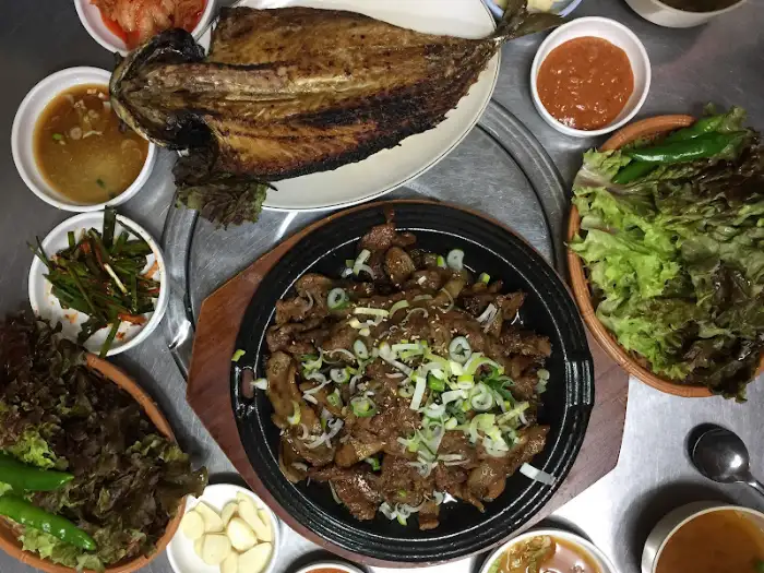 식탁 위에 차려진 푸짐한 한 상차림, 돼지불백과 생선구이, 쌈 채소 등