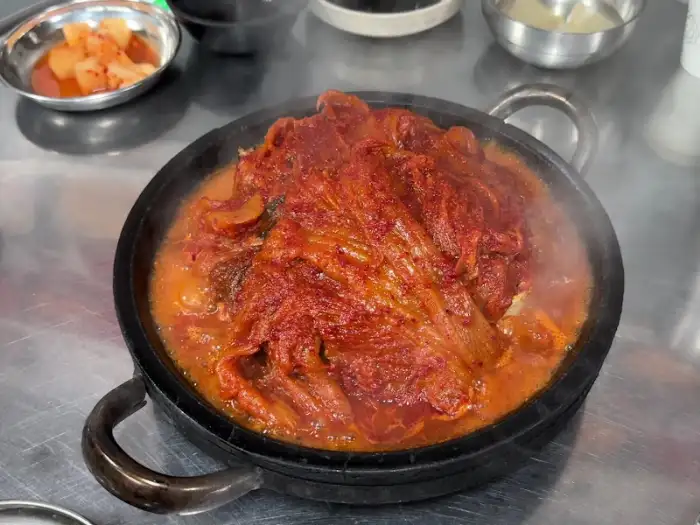 돌판 위에 끓고 있는 묵은지 고등어조림. 붉은 양념과 묵은지, 고등어가 어우러져 있다.