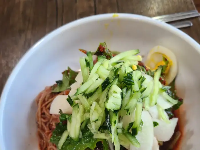 비빔막국수로 보이는 음식 위 상큼한 오이채와 계란