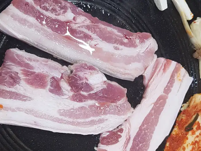 신선하고 두툼한 삼겹살 덩어리가 불판 위에 놓여 있는 모습
