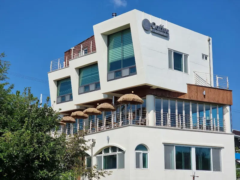 카페 외관 사진, 하얀색 건물에 테라스 좌석이 마련되어 있다.