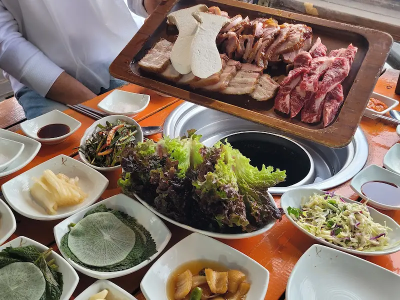 다양한 쌈 채소와 곁들임 반찬, 그리고 메인 메뉴인 고기가 푸짐하게 차려진 테이블