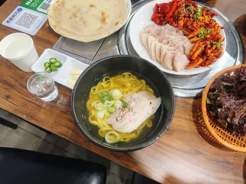 테이블 위에 놓인 오징어보쌈, 칼국수, 쌈 채소 등이 푸짐하게 차려져 있다.