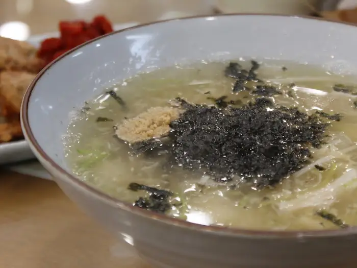 따뜻한 옹심이 국물 그릇의 클로즈업 사진. 얇게 썰린 파와 김가루가 국물 위에 떠있다.