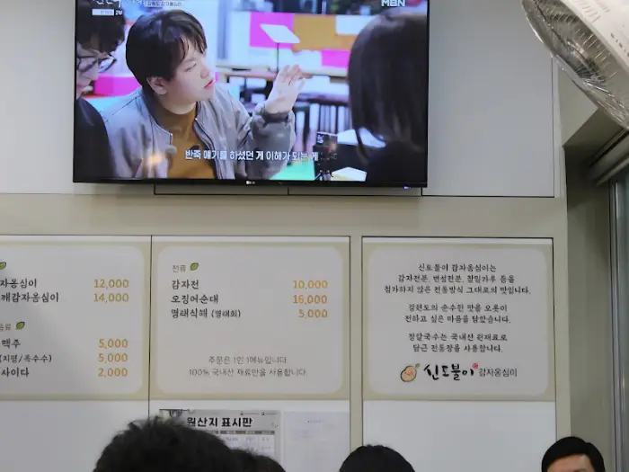 벽면에 걸린 TV 화면에는 방송 프로그램의 한 장면이 나오고, 그 아래에는 메뉴판과 함께 가게에 대한 설명이 적혀있다.