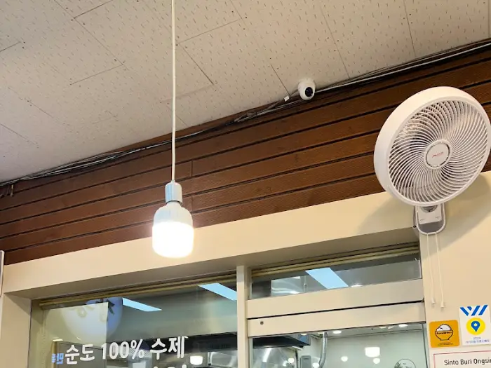 가게 천장에 달린 하얀 갓등과 벽면에 설치된 선풍기가 보인다. 심플한 조명과 환풍 시설이 눈에 띈다.