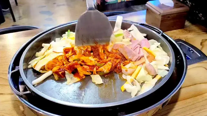 닭갈비에 양배추와 햄이 추가되어 철판에서 조리되는 모습