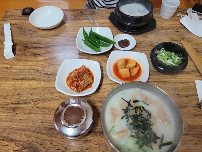 테이블에 차려진 설렁탕, 만두국, 김치, 깍두기, 고추 등의 음식 사진