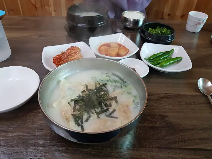 테이블에 차려진 만두국, 김치, 깍두기, 고추 등의 음식 사진