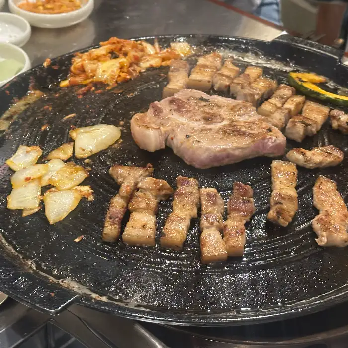 불판 위에서 노릇하게 구워지는 목살과 곁들임 채소