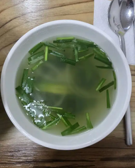 새하얀 그릇에 담긴 맑은 국물과 초록색 파