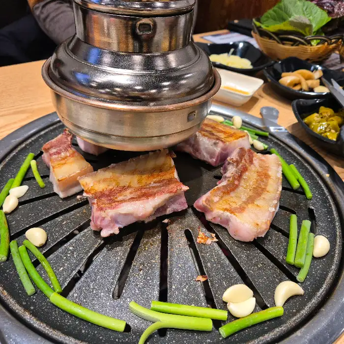 고기 굽는 불판 위에 놓인 삼겹살과 마늘, 풋고추