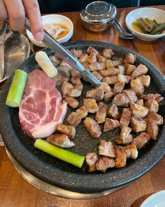 두툼한 삼겹살 덩어리와 함께 불판 위에 올려진 파와 마늘
