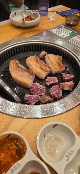 잘 구워진 삼겹살과 목살 조각들이 불판 위에 놓여 있다.