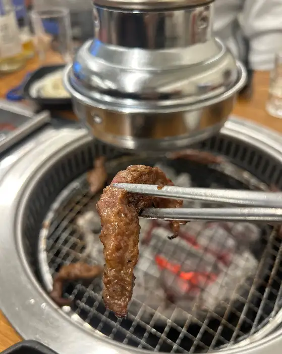 집게로 집어 올린 갈비살 한 점이 숯불 위에서 익어가고 있는 모습