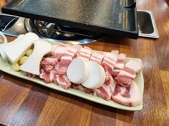 불판 위에 올려진 삼겹살과 버섯, 마늘, 양파