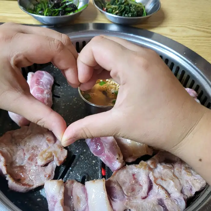 숯불 위에서 익어가는 고기와 하트 모양으로 맞댄 손