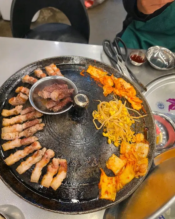 솥뚜껑 위에서 익어가는 삼겹살, 김치, 콩나물