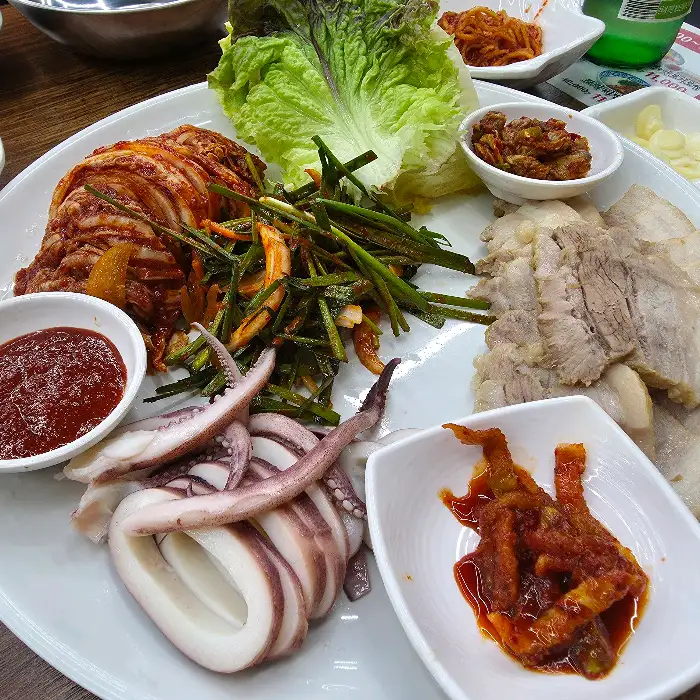 보쌈, 묵은지, 오징어, 쌈 채소가 함께 플레이팅된 모습