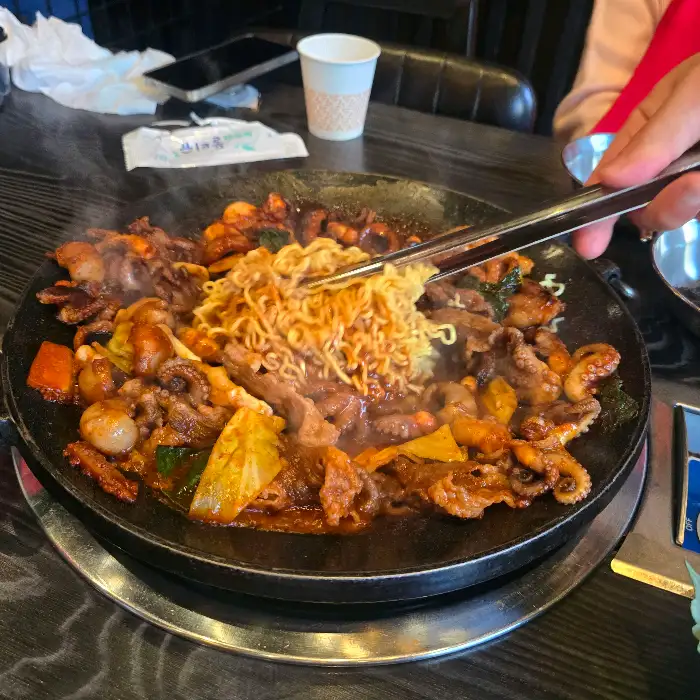 철판 위에서 쭈꾸미와 라면사리가 함께 볶아지고 있는 모습