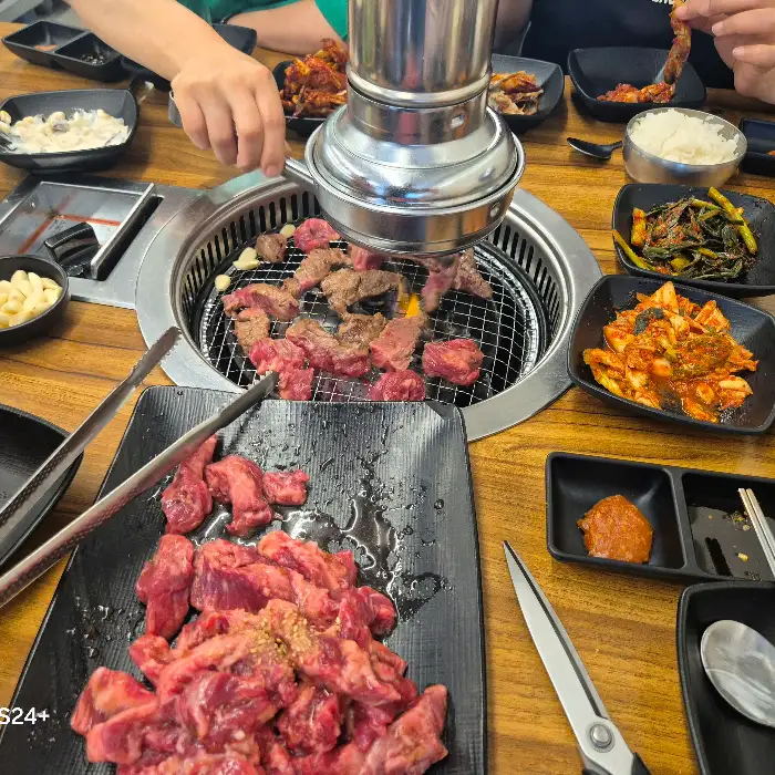 숯불 위에서 구워지고 있는 갈비살과 주변 반찬들