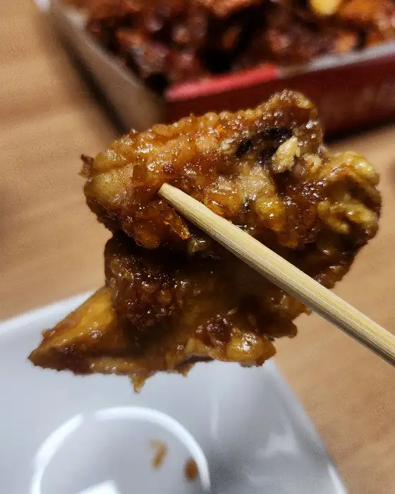 나무젓가락으로 집어 올린 칠리 양념 치킨 한 조각