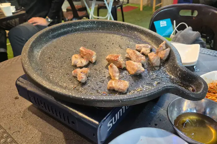 테이블 위에 놓인 불판과 그 위에 익고 있는 고기 조각들
