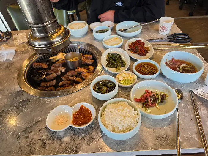 테이블 위에 차려진 다양한 반찬과 밥, 그리고 불판 위의 고기