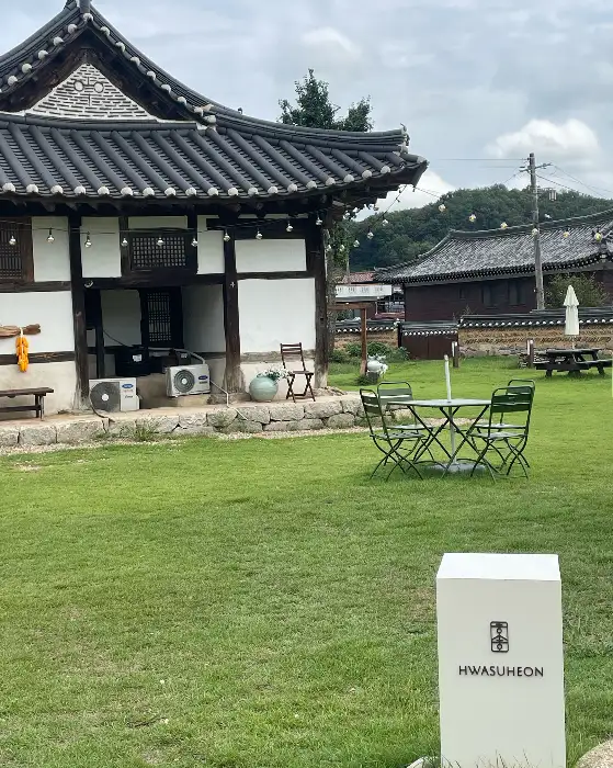 화수헌의 넓은 잔디 마당과 야외 좌석, 멀리 보이는 한옥 건물이 평화로운 분위기를 자아낸다.