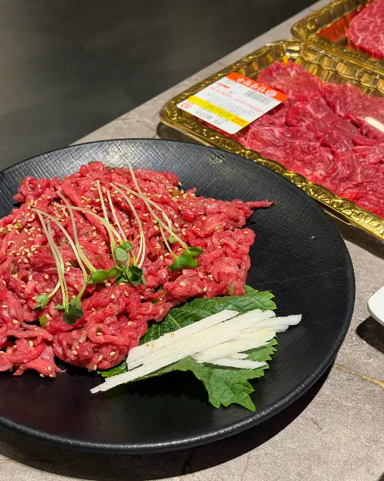 검은색 접시에 담겨 있는 신선한 육회와 곁들임 채소