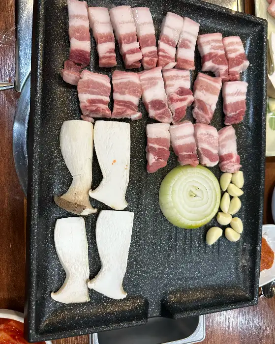 정사각형 모양의 불판에 정갈하게 담긴 삼겹살과 버섯