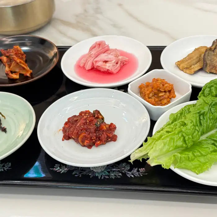 김치, 쌈 채소, 젓갈 등 다양한 곁들임 반찬들이 준비되어 있다.