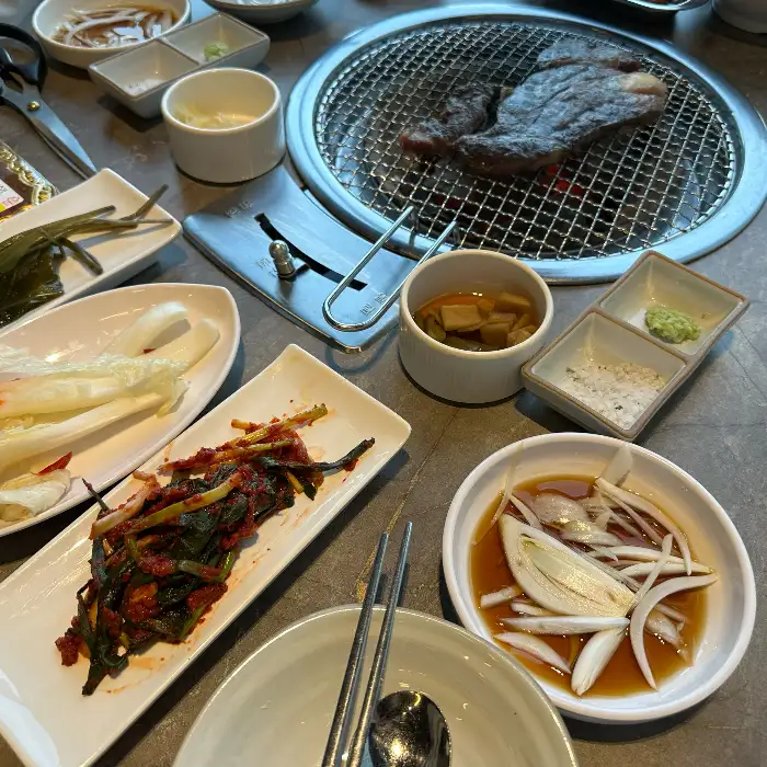 테이블 위에 놓인 숯불 위에서 익어가는 고기와 다양한 반찬들